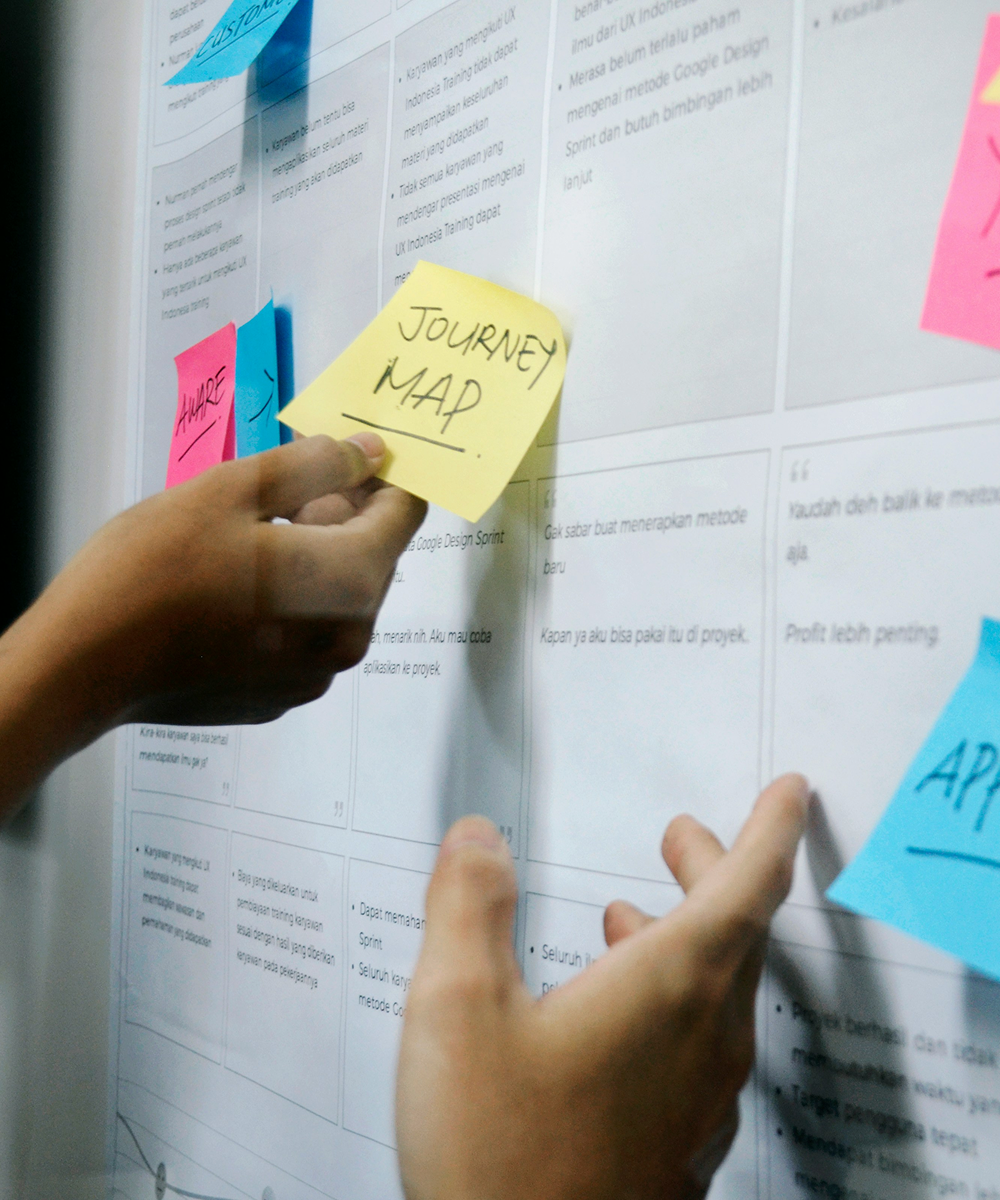 Close up image of a person brainstorming by putting post-it notes onto a whiteboard.